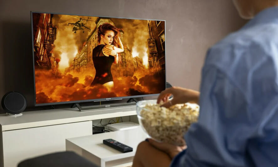 a person eating popcorns and watching the movie on tv