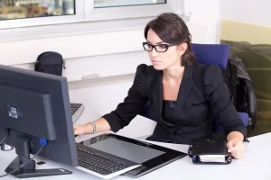 a woman sittng at the desk in front of the monitor