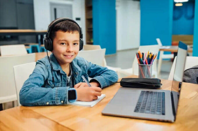 a boy with headphones sitting in front of the laptop