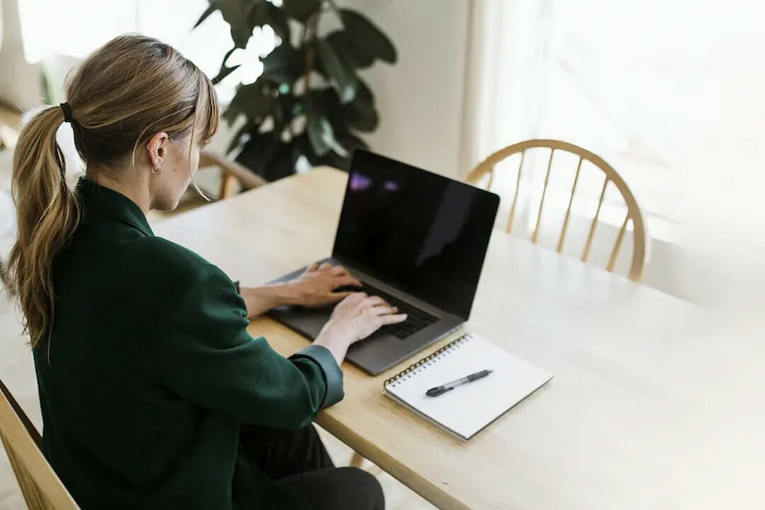 a woman sitting at the table and typing on laptop