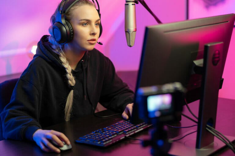 A blonde girl sitting at her pc and wearing headphones