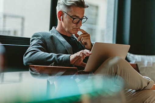 Man with glasses siting and holding a laptop