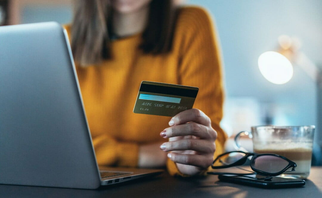 A person holding a credit card in front of the laptop